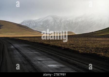 Eine ruhige Szene der riesigen Highlands in Island mit einer unbefestigten Straße, die sanft durch die karge Landschaft vor schneebedeckten Bergen führt Stockfoto