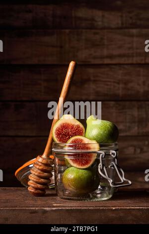 Ganze und in Scheiben geschnittene Feigen in einem Glas mit einem hölzernen Honiglöffel auf einem rustikalen Holzhintergrund für ein natürliches und gesundes Gefühl. Stockfoto