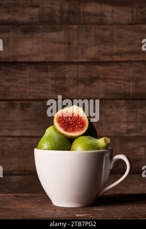 Ein rustikales Stillleben aus frischen grünen Feigen, eine in Scheiben geschnitten, um die rote Innenausstattung zu präsentieren, gepaart mit einem hölzernen Honiglöffel, alles wunderschön angeordnet Stockfoto