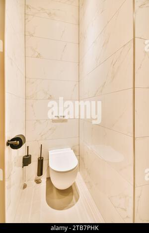 Das Innere des kleinen, sauberen Badezimmers ist mit einer keramischen Toilettenschale umgeben, die von weißen gefliesten Wänden in einem modernen Apartment umgeben ist Stockfoto