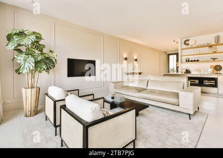 Sofa mit Sesseln und Couchtisch vor dem Fernseher im geräumigen Wohnzimmer mit weißen Wänden in einem modernen Apartment Stockfoto