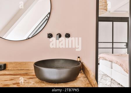 Spiegel mit Knöpfen und Wasserhähnen an der rosafarbenen Wand mit schwarzem Waschbecken auf Holzoberfläche im modernen Badezimmer Stockfoto