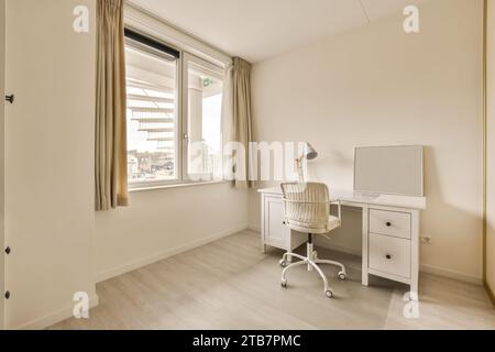 Weißer Schreibtisch und Stuhl mit Lampe und Spiegel am Fenster mit Vorhängen in einem modernen, geräumigen Apartment Stockfoto
