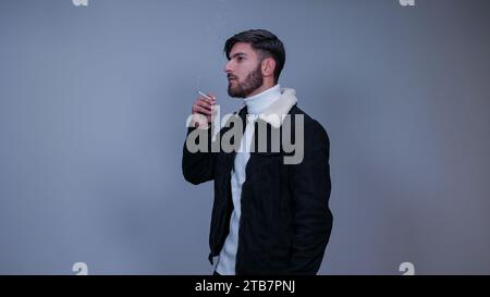 Ein junger Mann raucht Zigaretten vor grauem Hintergrund. Stockfoto
