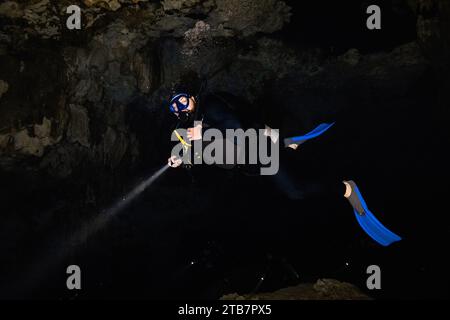 Ein ganzer Körper anonymer Taucher mit Flossen, Tauchausrüstung und Taschenlampe, der in die Kamera blickt, während er inmitten einer aufregenden Entdeckungsreise schwimmt Stockfoto