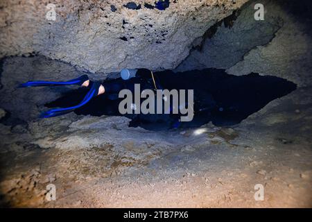 Rückansicht anonymer Unterwasserforscher mit Flossen und Tauchausrüstung, die durch die ruhige Dunkelheit des Cenote Dos Ojos in Mexiko navigieren, umgeben von der CA Stockfoto