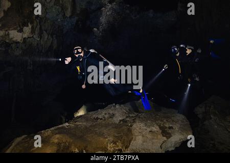 Seitenansicht einer Gruppe anonymer Taucher mit Flossen, Tauchausrüstung und Taschenlampen, die in die Kamera schauen, während sie inmitten eines aufregenden E schwimmen Stockfoto