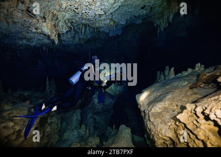 Seitenansicht einer Gruppe anonymer Taucher, vor den komplexen Texturen der Cenote Dos Ojos in Mexiko, die durch enge Gänge schwimmen Stockfoto