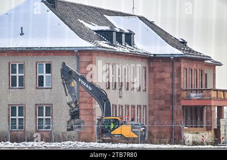 05. Dezember 2023, Brandenburg, Schönefeld: Blick durch einen Zaun eines Baggers vor dem General Hotel auf dem ehemaligen Flugplatz Schönefeld, dem heutigen Flughafen Berlin Brandenburg (BER), der zum Abbruch geplant ist. Nach wochenlangen Vorbereitungsarbeiten soll im Dezember der Abriss des historischen General Hotels auf dem BER-Flughafengelände beginnen. Das ehemalige Empfangsgebäude für Vertreter der Sowjetunion und Staatsgäste der DDR wurde seit Mitte September entkernt. Foto: Patrick Pleul/dpa Stockfoto