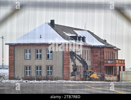 05. Dezember 2023, Brandenburg, Schönefeld: Blick durch einen Zaun eines Baggers vor dem General Hotel auf dem ehemaligen Flugplatz Schönefeld, dem heutigen Flughafen Berlin Brandenburg (BER), der zum Abbruch geplant ist. Nach wochenlangen Vorbereitungsarbeiten soll im Dezember der Abriss des historischen General Hotels auf dem BER-Flughafengelände beginnen. Das ehemalige Empfangsgebäude für Vertreter der Sowjetunion und Staatsgäste der DDR wurde seit Mitte September entkernt. Foto: Patrick Pleul/dpa Stockfoto