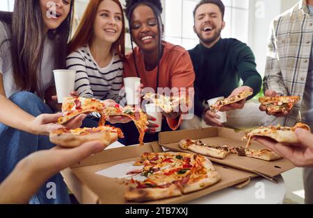 Fröhliche Freunde, die sich zu Hause treffen und Pizza essen, miteinander reden und lachen Stockfoto