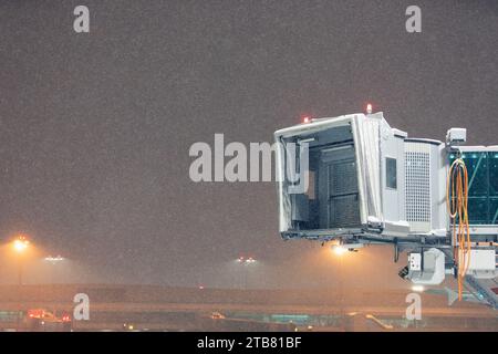 Winter frostige Nacht am Flughafen bei starkem Schneefall. Illiminierte leere Passagierbrücke vor dunklem Himmel mit Schneeflocken. Stockfoto