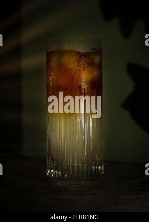 Dunkler und stürmischer Highball-Cocktail mit Eis und Limette vor grünem Hintergrund Stockfoto
