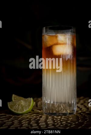 Dunkler und stürmischer Highball-Cocktail mit Eis und Limette vor grünem Hintergrund Stockfoto