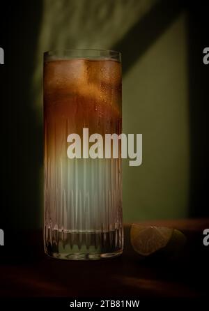 Dunkler und stürmischer Highball-Cocktail mit Eis und Limette vor grünem Hintergrund Stockfoto