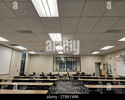 Ein leerer Innenraum mit Schreibtischreihen und einem von der Decke abgehängten Projektor Stockfoto
