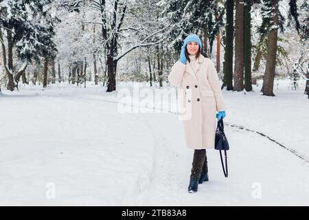 Ganzkörperporträt einer jungen Frau, die im verschneiten Winterpark mit weißem Pelzmantel läuft. Warme Kleidung für kaltes Wetter Stockfoto