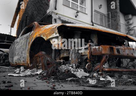 Ein verbranntes zerstörtes Auto in der Nähe eines zivilen Gebäudes. Das Ergebnis von Mörserbeschuss während des russisch-ukrainischen Krieges. Stockfoto