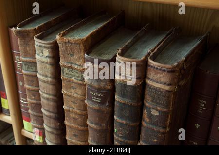 Staubige, abgenutzte und verblasste jüdische Heiligbücher, die in Leder gebunden sind, stehen aufrecht auf einem Bücherregal. Stockfoto