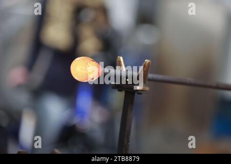 Derenburg, Deutschland. Dezember 2023. Am Schmelzofen wird ein Stück Glas gebildet. Die Glasmanufaktur Harzkristall GmbH ist eine der wenigen Glaswerke in Deutschland, die mundgeblasene Produkte herstellt. Es ist spezialisiert auf Vasen, Glaslampen, die Herstellung von Glasteilen und Lampen für denkmalgeschützte Gebäude sowie Glaskunstprodukte in Zusammenarbeit mit renommierten Künstlern. Das Unternehmen produziert seit 70 Jahren Glasprodukte. Ein besonderer Magnet ist eine Weihnachtsausstellung mit verschiedenen Glasprodukten für die Adventszeit. Quelle: Matthias Bein/dpa/Alamy Live News Stockfoto