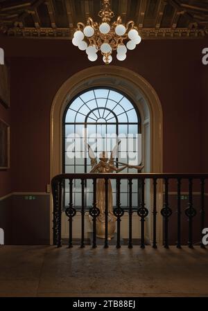 London, Großbritannien - 27. November 2023 - Blick auf die Angel-Statue vor dem Holzfenster an der roten Wand des Victoria and Albert Museum. Abstrakte Innenarchitektur, Sp Stockfoto