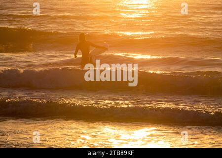 Vielle-Saint-Girons (Südwestfrankreich): Junge Frau, Surferin, die bei Sonnenuntergang in die Wellen des Atlantischen Ozeans einsteigt Stockfoto