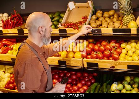 Bärtiger, reifer Verkäufer, der im Lebensmittelgeschäft lebhaftes Obst und Gemüse mit Preisschildern versehen hat Stockfoto