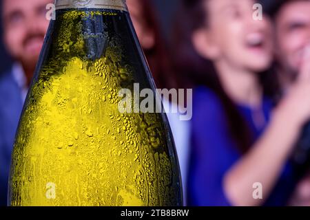 Eine taufende Flasche alkoholischen Getränks mit fröhlich verschwommenen Leuten im Hintergrund Stockfoto