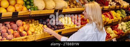 Fröhlich reife Frau in lässigen Kleidern mit Einkaufstasche, die Obst im Supermarkt auswählt, Banner Stockfoto