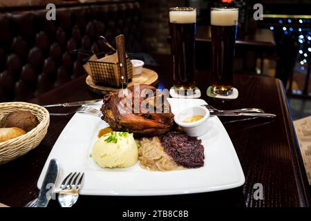 Gebackener Schweineschaft mit Sauerkraut und Kartoffelpüree auf einem Holztisch. Eine große Portion gegrilltes Schweinefleisch und Bier auf dem Tisch im Pub. Stockfoto