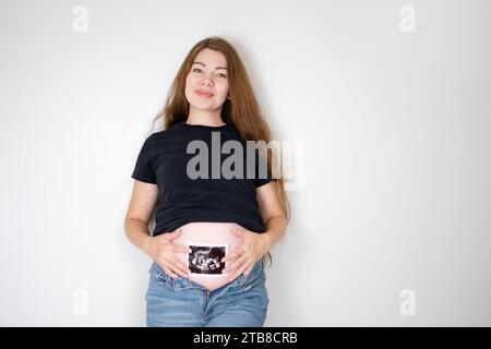 Schwangere kaukasische Frau mit langen Haaren, die ein Sonogrammbild hält. Das Ultraschallbild des Babys. 22 Wochen schwanger Stockfoto