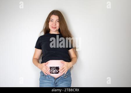 Schwangere kaukasische Frau mit langen Haaren, die ein Sonogrammbild hält. Das Ultraschallbild des Babys. 22 Wochen schwanger Stockfoto