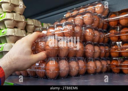 Hühnereier im Ladenregal. Ein Kunde nimmt eine Verpackung mit Hühnereiern aus einem Supermarkt-Kühlschrank. Behälter mit Hühnereiern im Kühlschrank Stockfoto