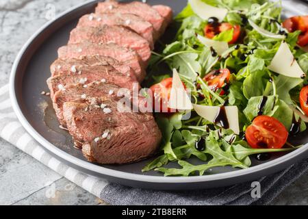 Italienischer Tagliata-Rindfleisch-Salat mit wilder Rakete, Kirschtomaten und Parmesankäse in Nahaufnahme auf einem Teller auf dem Tisch. Horizontal Stockfoto