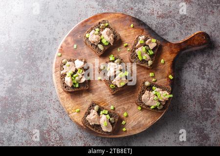 Gesundes Roggenbrot mit Dosenleber, Kapern und grünen Zwiebeln Nahaufnahme auf einem Schneidebrett auf dem Tisch. Horizontale Draufsicht von oben Stockfoto