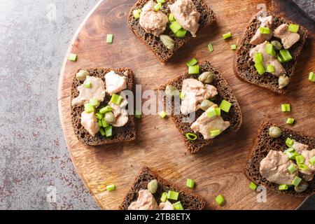 Leckere Sandwiches mit Kabeljauleber, Kapern und grünen Zwiebeln in Nahaufnahme auf einem Holzbrett auf dem Tisch. Horizontale Draufsicht von oben Stockfoto
