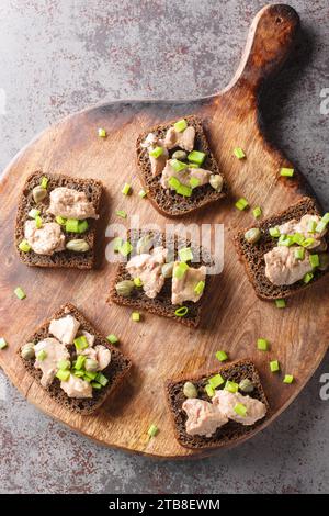 Roggentoast mit Kabeljauleber, grünen Zwiebeln und Kapern in Nahaufnahme auf einem Holzbrett auf dem Tisch. Vertikale Draufsicht von oben Stockfoto
