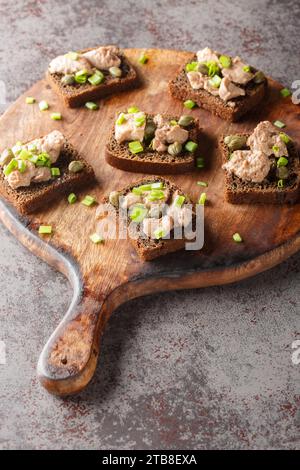 Sandwiches mit Kabeljauleber aus der Dose, grünen Zwiebeln und Kapern in Nahaufnahme auf einem Holzbrett auf dem Tisch. Vertikal Stockfoto