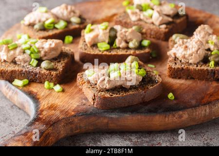 Leckere Sandwiches mit Kabeljauleber, Kapern und grünen Zwiebeln in Nahaufnahme auf einem Holzbrett auf dem Tisch. Horizontal Stockfoto