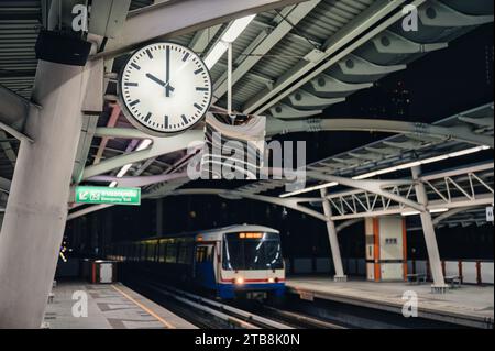 Skytrain kommt nachts auf dem Bahnsteig und der großen Uhr in der Metropole Bangkok an Stockfoto
