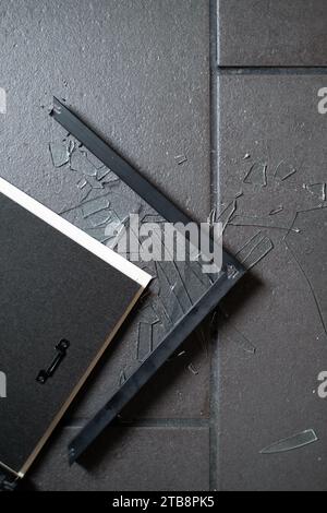 Ein gebrochener Bilderrahmen auf einem gefliesten Boden, der Rahmen selbst an den Fugen gebrochen und das Glas zertrümmert. Stockfoto