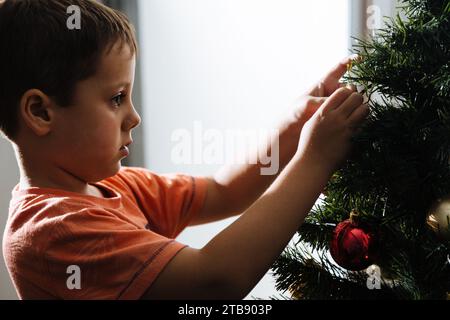 Der Junge, der den weihnachtsbaum in seinem Haus vor der Weihnachtsfeier zusammenstellt. Stockfoto