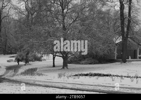 Blick auf den Wintry Park, mit einem schneebedeckten Baum und einem gewundenen Pfad. Ein entfernter Mensch bringt Leben in die heitere Winterszene, Harrogate, Großbritannien. Stockfoto