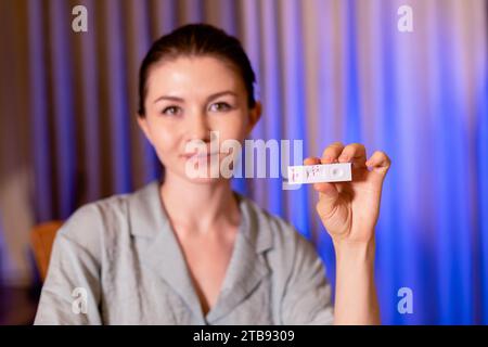 Nahaufnahme einer glücklichen Frau mit Schnelltestgerät mit negativem COVID-19-Ergebnis zu Hause. Konzentrieren Sie sich auf ein Gerät Stockfoto