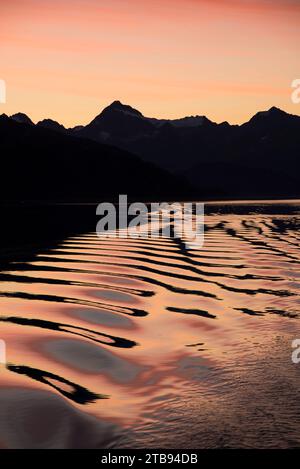 Wunderschöner Sonnenuntergangshimmel über der Glacier Bay mit den Wellen eines kleinen Bootes, das über das Wasser fährt, in Passage, Alaska, USA Stockfoto