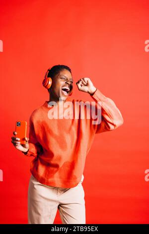 Glückliche junge Frau, die im Studio tanzt und singt, während sie kabellose Kopfhörer trägt. Frau, die ihre Lieblingsmusik-Playlisten hört. Stockfoto