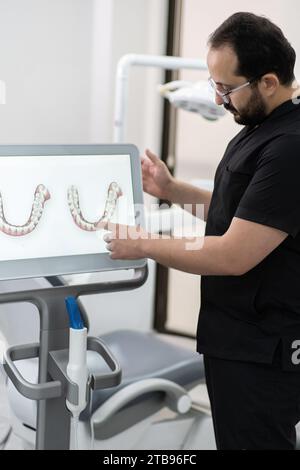 Spezialist für Uniform-Zeigen auf Kiefermodelle auf Computerbildschirmen mit alternativer Zahnbehandlung Stockfoto