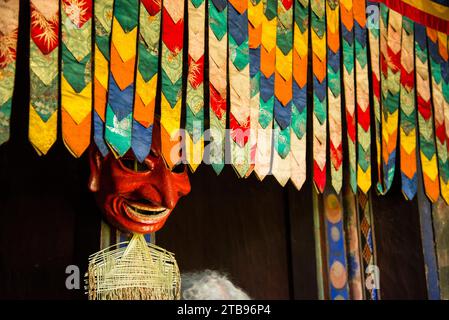 Maske in einem Bauernhaus hinter hängendem bunten dekorativen Stoff; Paro Valley, Bhutan Stockfoto