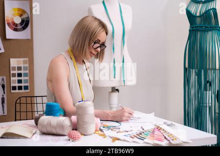 Frau mit Brille arbeitet an eleganten Kleidungsskizzen in Modestudios, Modedesignern im Studio Stockfoto