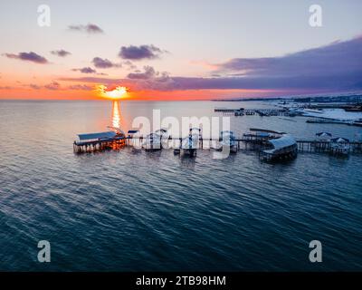 Blick aus der Vogelperspektive auf den fantastischen farbenfrohen Sonnenuntergang über dem Meer mit riesigen Wolken und Silhouette des Piers Stockfoto